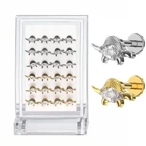 Assorted G23 titanium stegosaurus labret studs with crystal detailing in silver and gold finishes shown on display stand with close-up design variations for piercing jewelry collection.